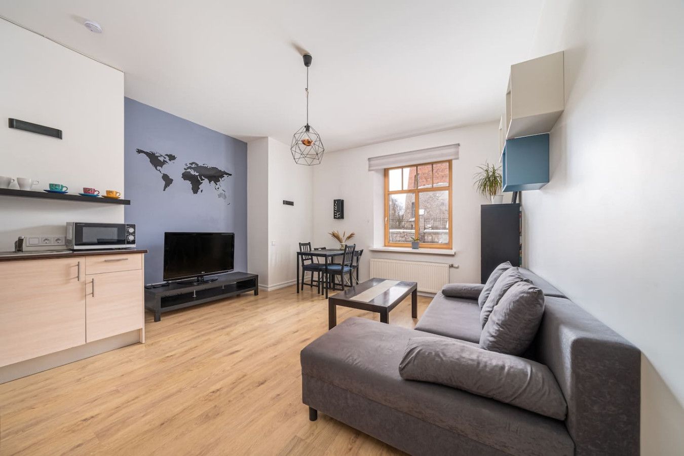 A modern living room with a grey sofa, a flat-screen TV, a dining table with chairs, and a world map on the wall.