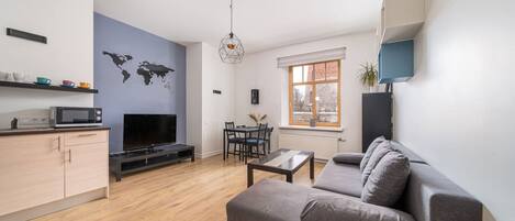 A modern living room with a grey sofa, a flat-screen TV, a dining table with chairs, and a world map on the wall.