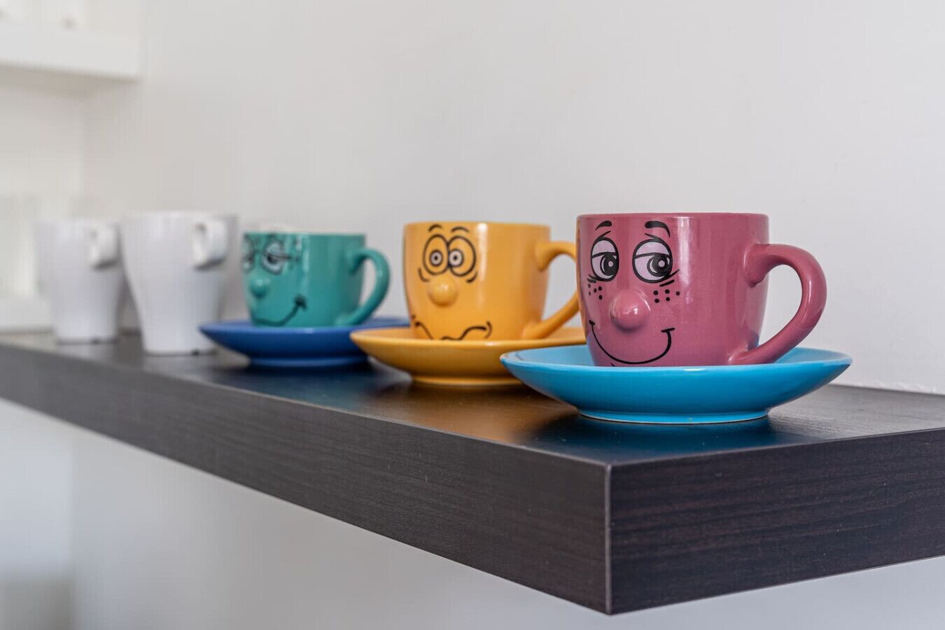 A row of colorful ceramic cups and saucers on a dark wooden shelf.