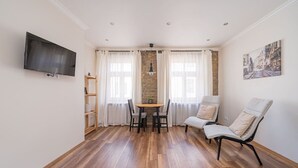 Ein Zimmer mit Holzboden, einem Esstisch mit Stühlen, einer Couch, einem an der Wand befestigten Fernseher und einem Gemälde.