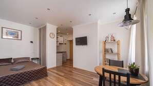 Ein gemütlicher Wohnraum mit Bett, Esstisch, Stuhl, Bücherregal und Fernseher.