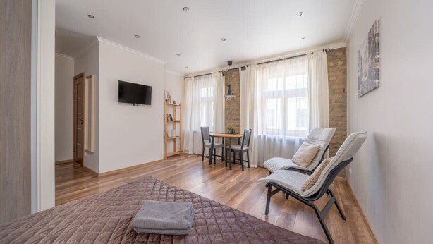 Ein geräumiges Zimmer mit einem Bett, einem Fernseher, einem Essbereich und einem Fenster mit Vorhängen.