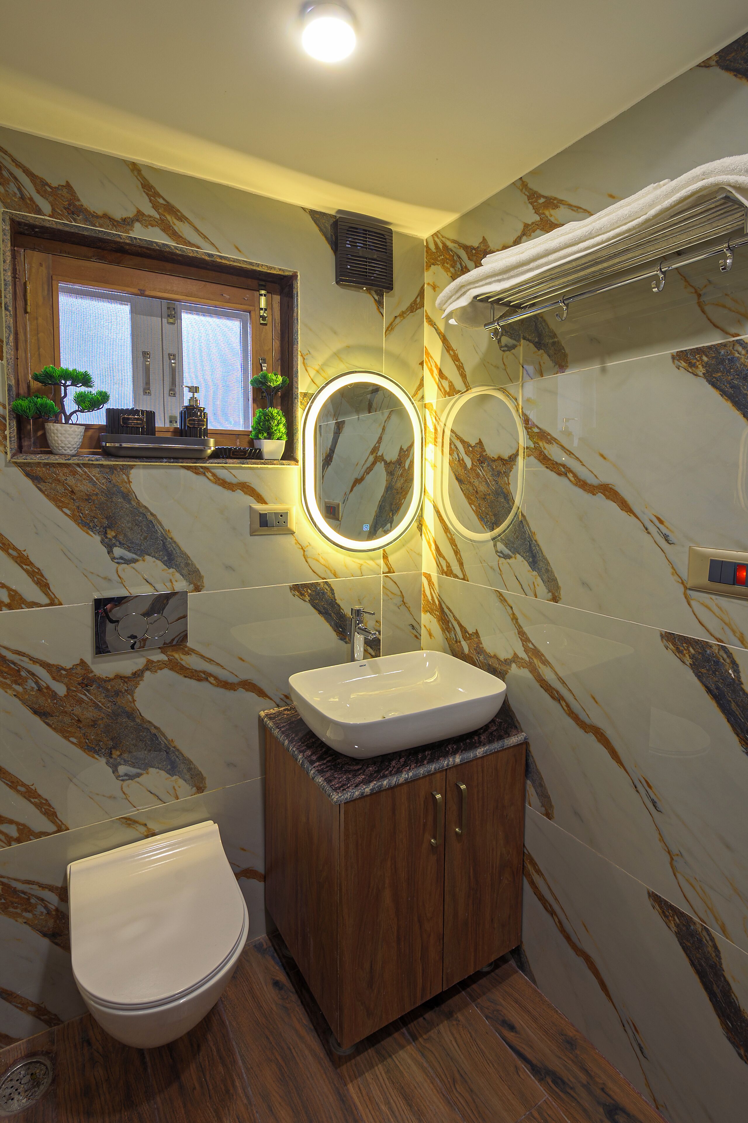 Un baño con pared de mármol, lavamanos, inodoro y espejo.