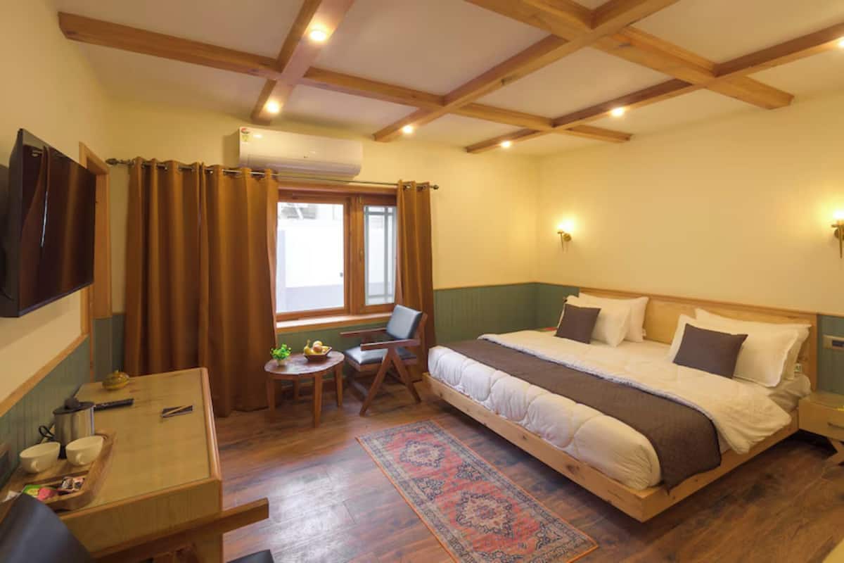 A bedroom with a bed, a desk, a chair, a small table, and a window with curtains.