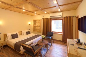 A cozy hotel room with a wooden ceiling, a large bed with a headboard, a wooden chair, a small table with a vase of flowers, and a television on the wall. - PalPenzy - Bespoke Premium Stay (Srinagar)