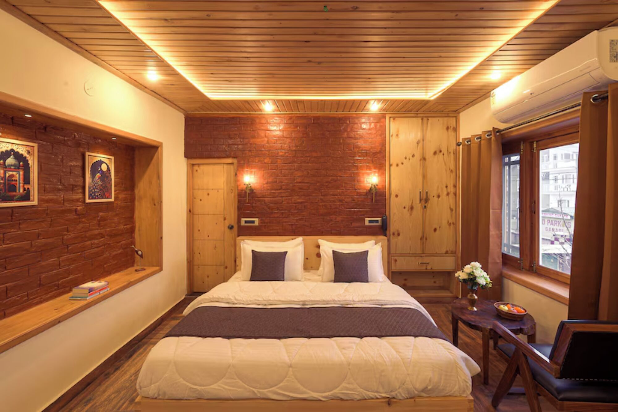 A bedroom with a brick wall, wooden ceiling, two beds, a nightstand, and a window with a view.