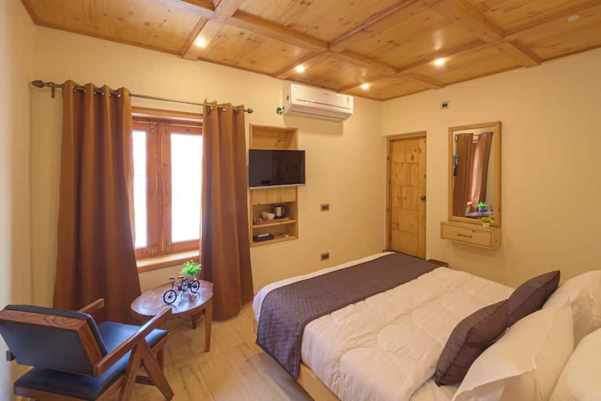 A bedroom with a bed, a desk, a chair, a television, and a window with curtains.