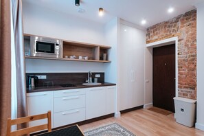 A compact kitchen with a microwave, sink, and wooden shelves. - Pernavas studio loft with free parking (Riga)