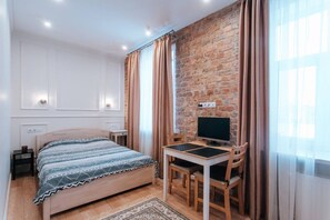 A bedroom with a bed, a desk with a computer, a brick wall, and a window with curtains. - Pernavas studio loft with free parking (Riga)
