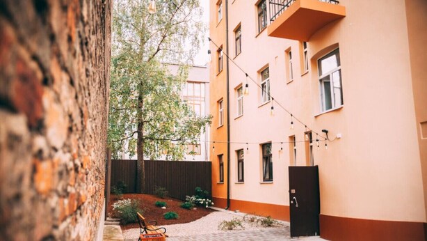 A narrow alleyway with a wooden bench, a small wooden box, and a tree. - Pernavas studio loft with free parking (Riga)