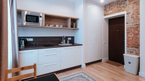A compact kitchen with a microwave, sink, and wooden shelves. - Pernavas studio loft with free parking (Riga)