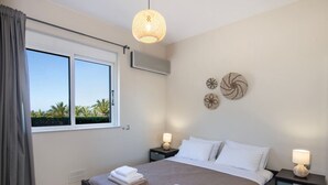 Une chambre à coucher comprenant un lit, deux tables de chevet, une fenêtre avec des rideaux, un appareil de climatisation et des éléments de décoration murale.