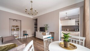 Una sala moderna con sofá, mesa de comedor y sillas, una zona de cocina con armarios y electrodomésticos, y un candelabro.