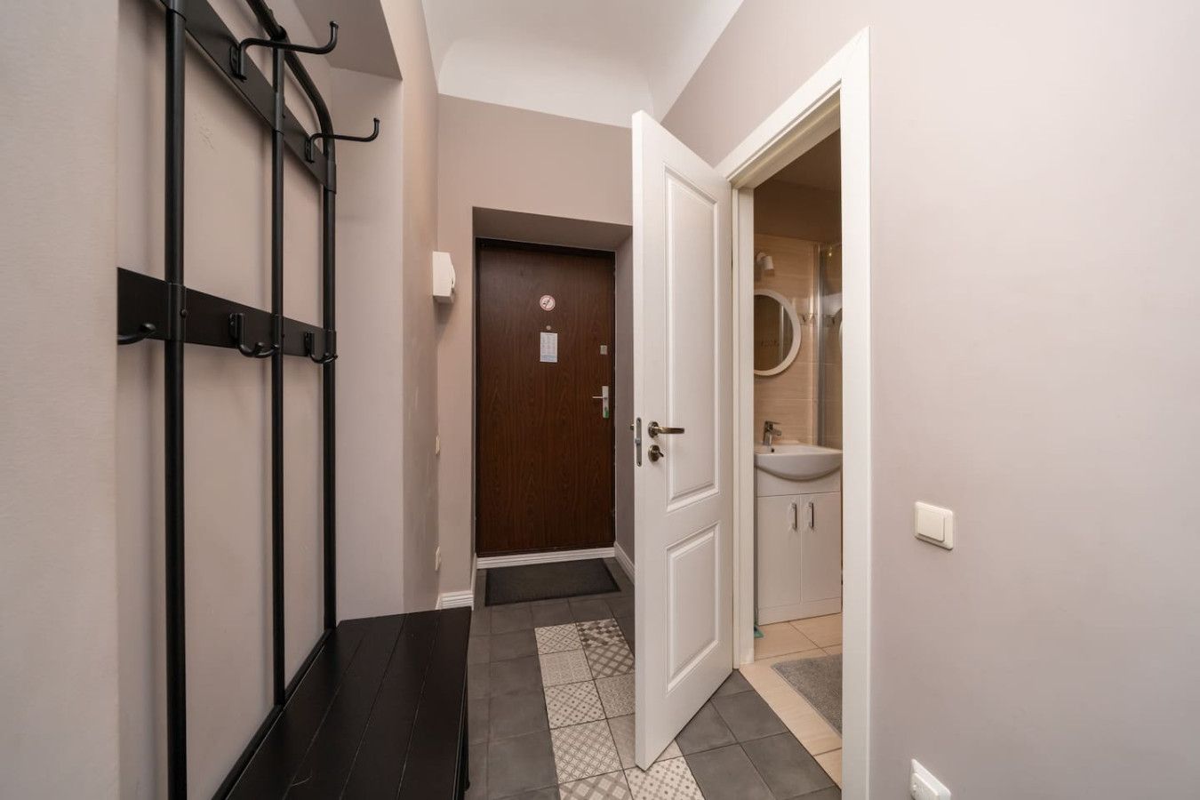 A hallway with a coat rack, a door leading to a bathroom, and a tiled floor.