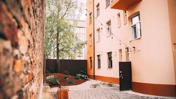 A courtyard with a wooden bench, a small planter, and a building with a balcony.