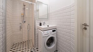 A bathroom with a glass-enclosed shower, a sink with a mirror above it, and a front-loading washing machine.