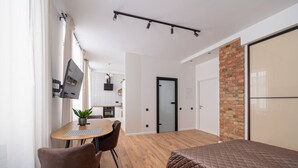 A modern bedroom with a large bed, a dining area with a table and chairs, a kitchen in the background, and a brick accent wall. - TOP location New high class furnishing 32 m2 (Riga)