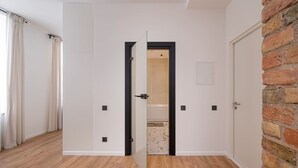Ein Zimmer mit Holzboden, weißen Wänden, einer Tür in Schwarzrahmen und einer Wand mit Backsteinverkleidung.