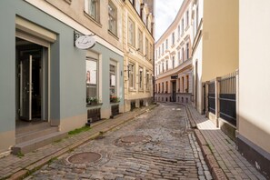 A narrow cobblestone street flanked by historic buildings with shopfronts and a visible sign for a salon. - TOP location New high class furnishing 32 m2 (Riga)