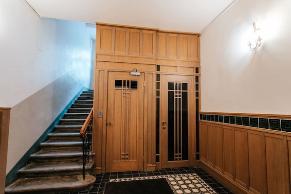 A staircase leading to a wooden door with a glass panel, a tiled floor, and a wall-mounted light fixture.