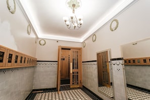 A bathroom with a tiled floor, a wooden door, a mirror, and a chandelier.