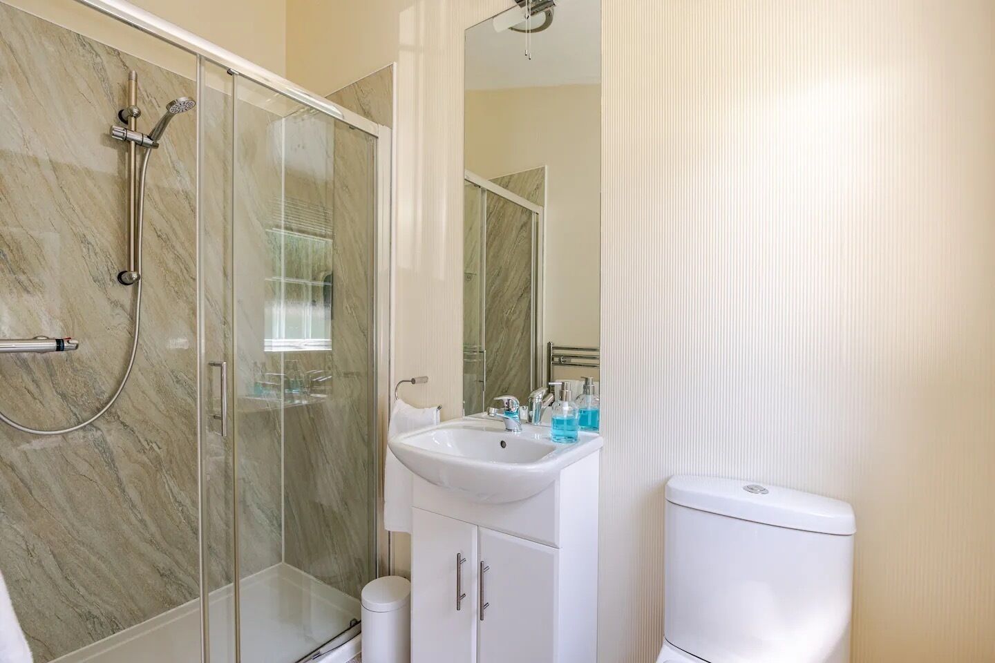 A modern bathroom with a glass-enclosed shower, a white sink, and a toilet.