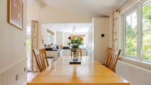 A long dining table with chairs, a vase with flowers, and a kitchen in the background. - Luxury lodge in peaceful surroundings (saltaash)