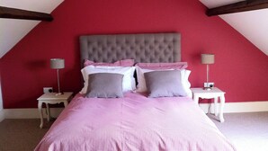 Une chambre avec un mur rouge, une tête de lit capitonnée, deux tables de chevet et un lit recouvert d’une couverture à carreaux.