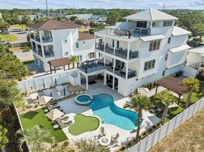 Um edifício residencial com vários andares, piscina, área de estar externa e um quintal cercado.