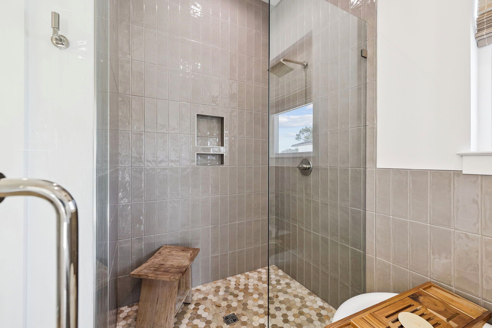 Une douche avec des portes en verre, un banc en bois et des toilettes dotées d’un plateau en bois.