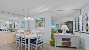 Une cuisine moderne avec des meubles blancs, une table à manger avec des chaises bleues et un vase vert.