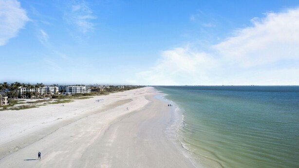 Une plage offrant une vue dégagée sur l’océan, avec une rangée de bâtiments en arrière-plan.