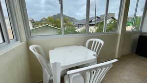 Un petit balcon avec une table et des chaises blanches, d’où l’on peut admirer les maisons et les montagnes à travers de grandes fenêtres.