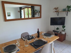 A dining room with a wooden table set for four, a TV mounted on the wall, and a mirror above the table.