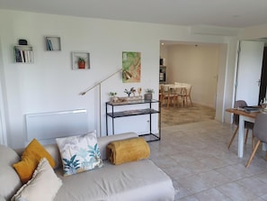 A living room with a sofa, a coffee table, a lamp, a map on the wall, and a dining area in the background.