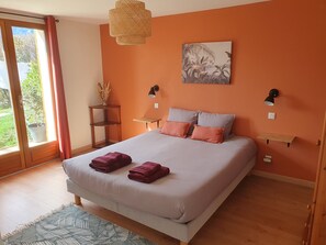 A bedroom with a large bed, two bedside tables, a wall-mounted lamp, a potted plant, and a view through a sliding door.