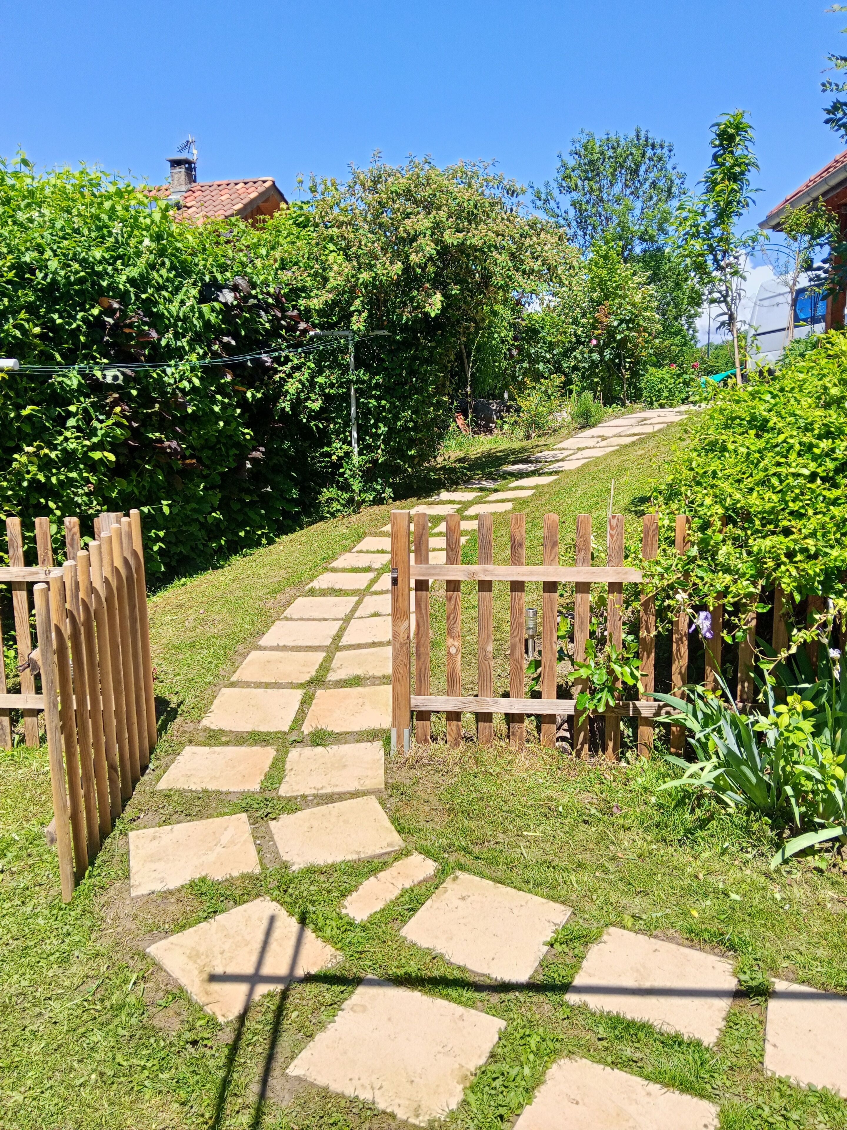Un sendero de piedra que atraviesa un jardín con cerca de madera y abundante vegetación.