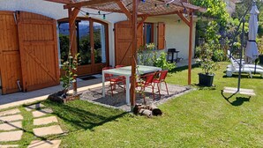 Eine Terrasse mit Tisch und Stühlen, eine Holz-Pergola, ein überdachter Bereich und Blick auf ein Haus.