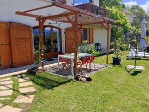 Une terrasse avec une table et des chaises, une pergola en bois, un espace couvert et une vue sur une maison.