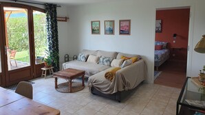 Ein Wohnzimmer mit einer Couch, einem Couchtisch, einem Esstisch und Blick ins Freie.