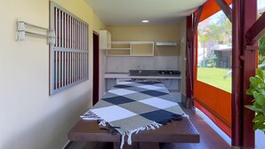 A room with a bed, a small kitchenette, a window with bars, and a view of greenery outside. - AP 40 Ala Bombinhas Residencial Solavir (Bombinhas)