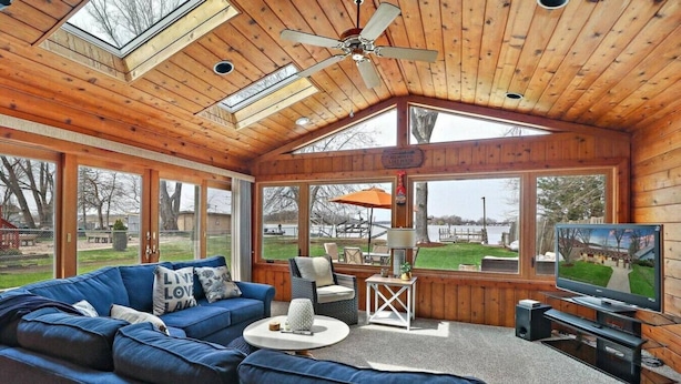 A cozy cabin with a large blue sofa, a television, and a ceiling fan. - Pet Friendly Sunset Lakefront Cottage in Fox Lake w/ Boat Pier (Fox Lake)