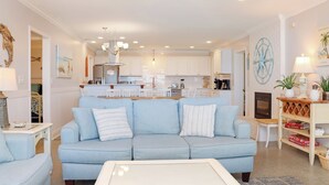 A modern living room with a light blue sofa, a white coffee table, and a kitchen in the background. - 🌞Steps from the Beach-Pet Friendly-Fab Beach Views-4BR Deja Blue🌞 (Mexico Beach)