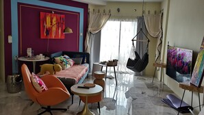 A modern living room with a sofa, orange chair, round coffee table, and a hanging chair.