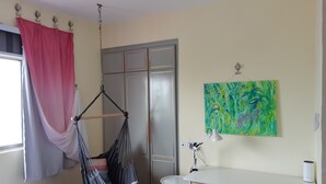 A room with a bed, a desk, a hanging chair, a wardrobe, and a painting.