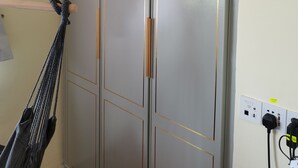 A grey wardrobe with gold trim and a macrame hanging in the corner.