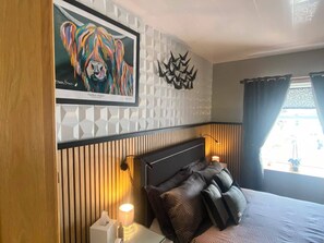 A hotel room with a bed, a framed artwork, a geometric wall design, and a window with curtains.