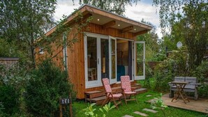A wooden cabin with a glass door, a deck, and outdoor seating. - Charming Chalet in Sint Maartenszee (Sint Maartensvlotbrug)