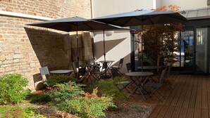 An outdoor patio with tables and chairs, surrounded by plants and a wooden deck. - Hôtel des Halles (Dijon)