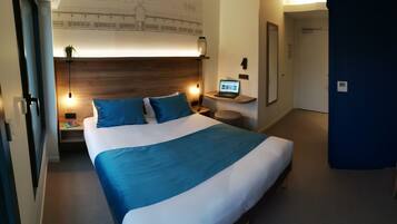 A hotel room with a bed, a desk with a laptop, a chair, and a large mirror.